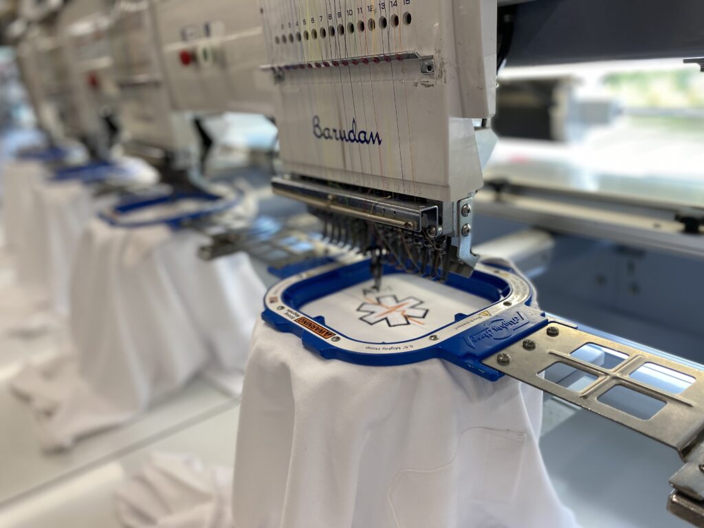 IMG_9570 - KM Concept Embroidery machine in operation with multiple thread colors and a fabric hoop labeled Barudan